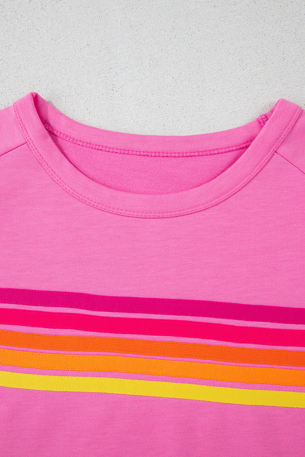 Close-up of the crew neckline and colorful striped chest detail on a pink casual T-shirt.