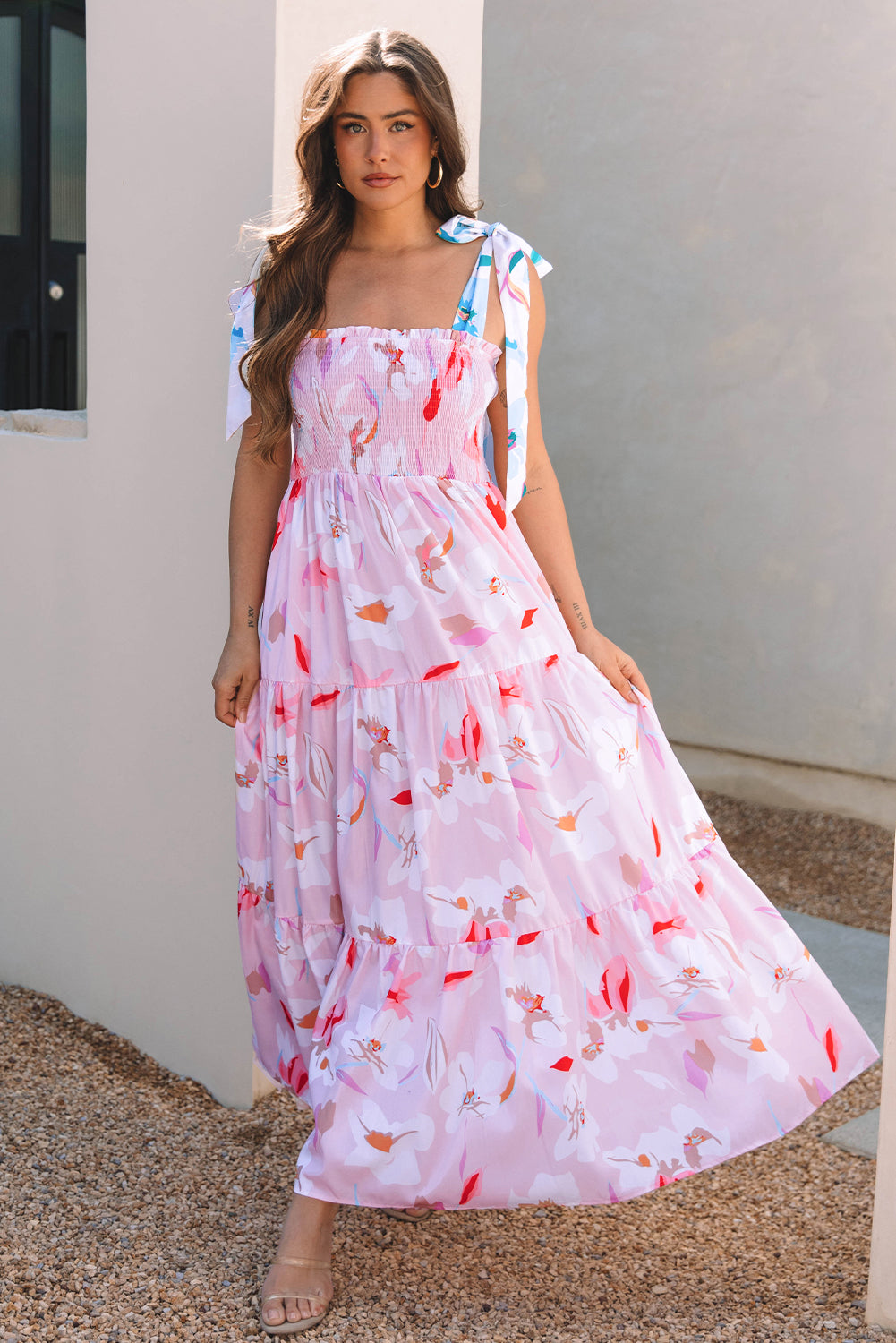 Woman wearing a pink floral sleeveless maxi dress with a tiered flowy skirt and feminine spring style.