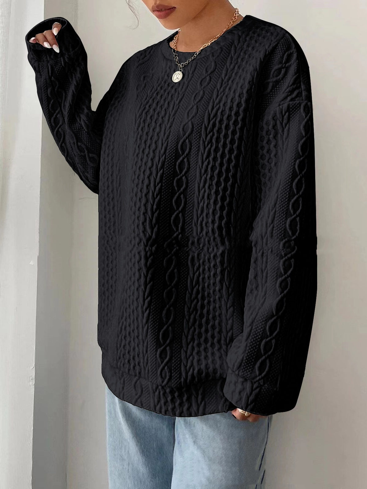 Woman wearing black cable-knit oversized sweater with jeans, front view
