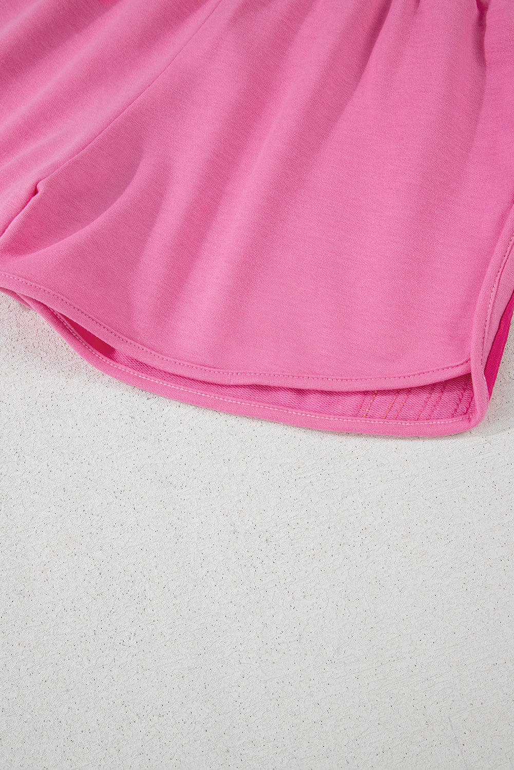 Close-up of the lightweight fabric and curved hem on pink women's athletic shorts.