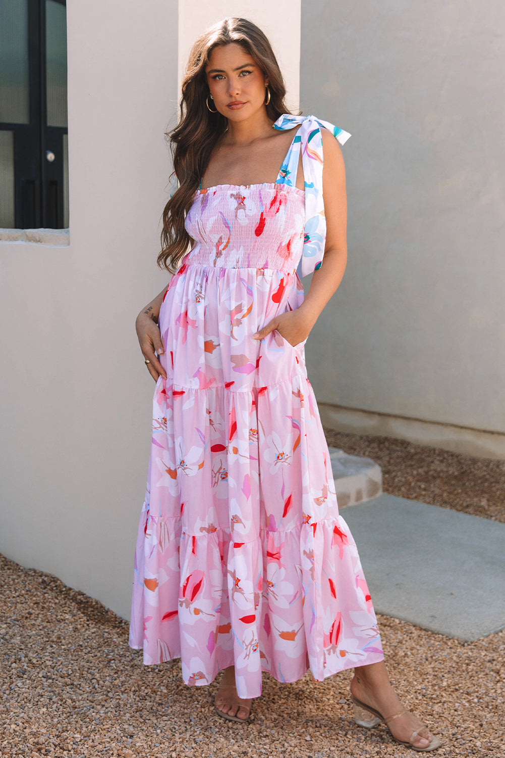 Model posing in a pink floral tiered maxi dress with a sleeveless neckline and relaxed, feminine silhouette.